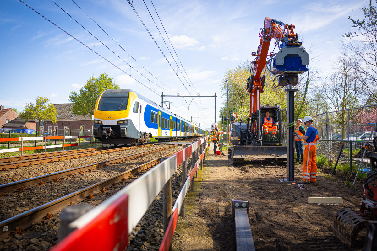 Fundering voor de nieuwe geluidsschermen langs het spoor bij Helvoirt wordt aangebracht terwijl een trein passeert richting 's-Hertogenbosch