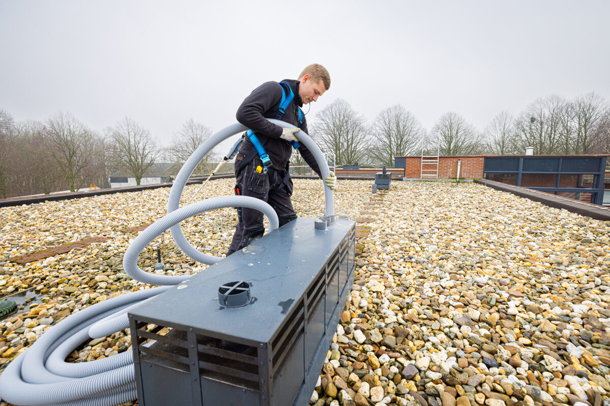 Een medewerker is bezig met een rookgasinstallatie op het dak van een appartementencomplex