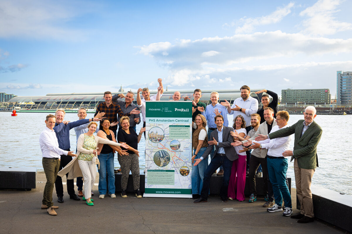 Een grote groep betrokken medewerkers van het project PHS Amsterdam Centraal met op de achtergrond het Centraal Station en 't IJ