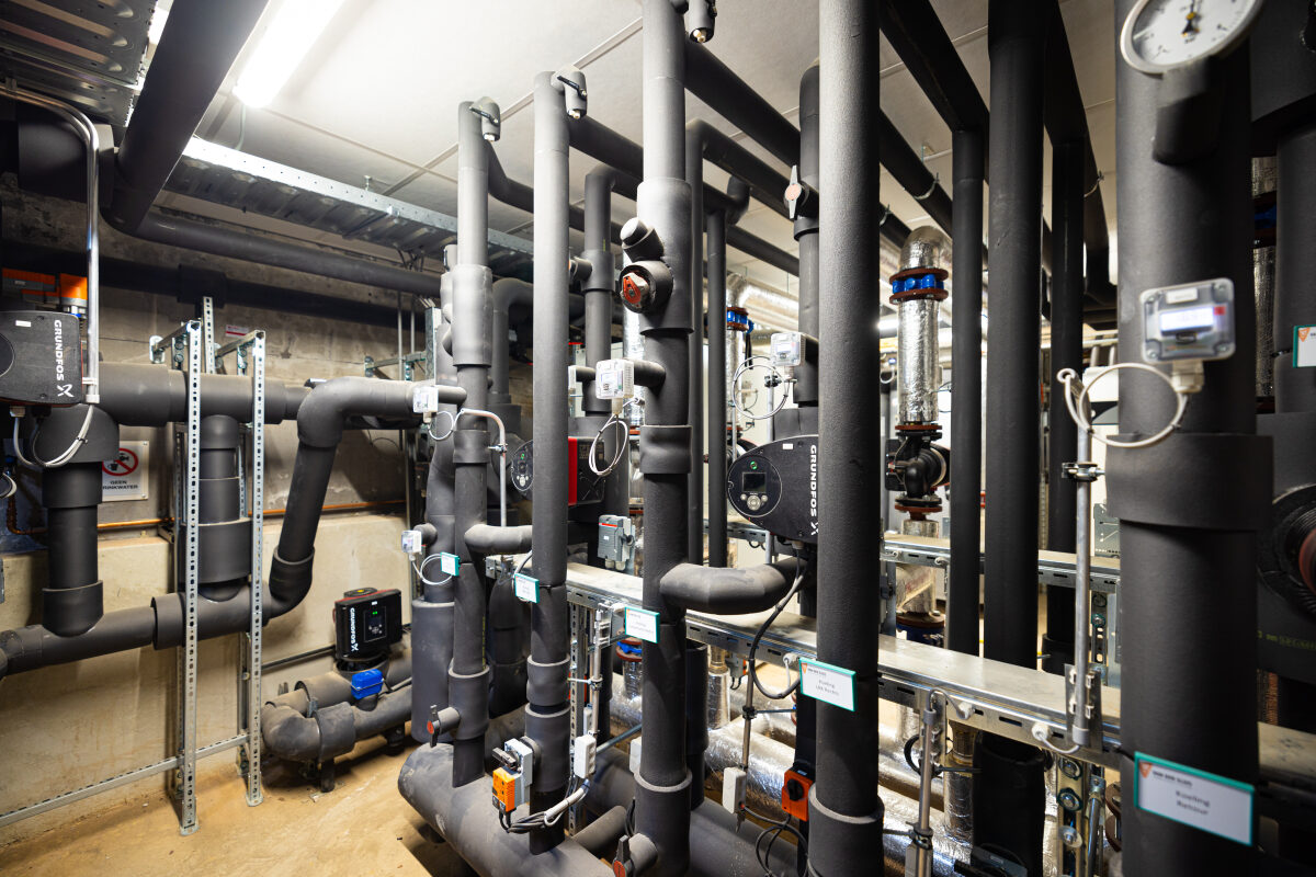 Een hoop metertjes en buizen bij de technische installaties voor klimaatbeheersing in een appartementencomplex in Kampen